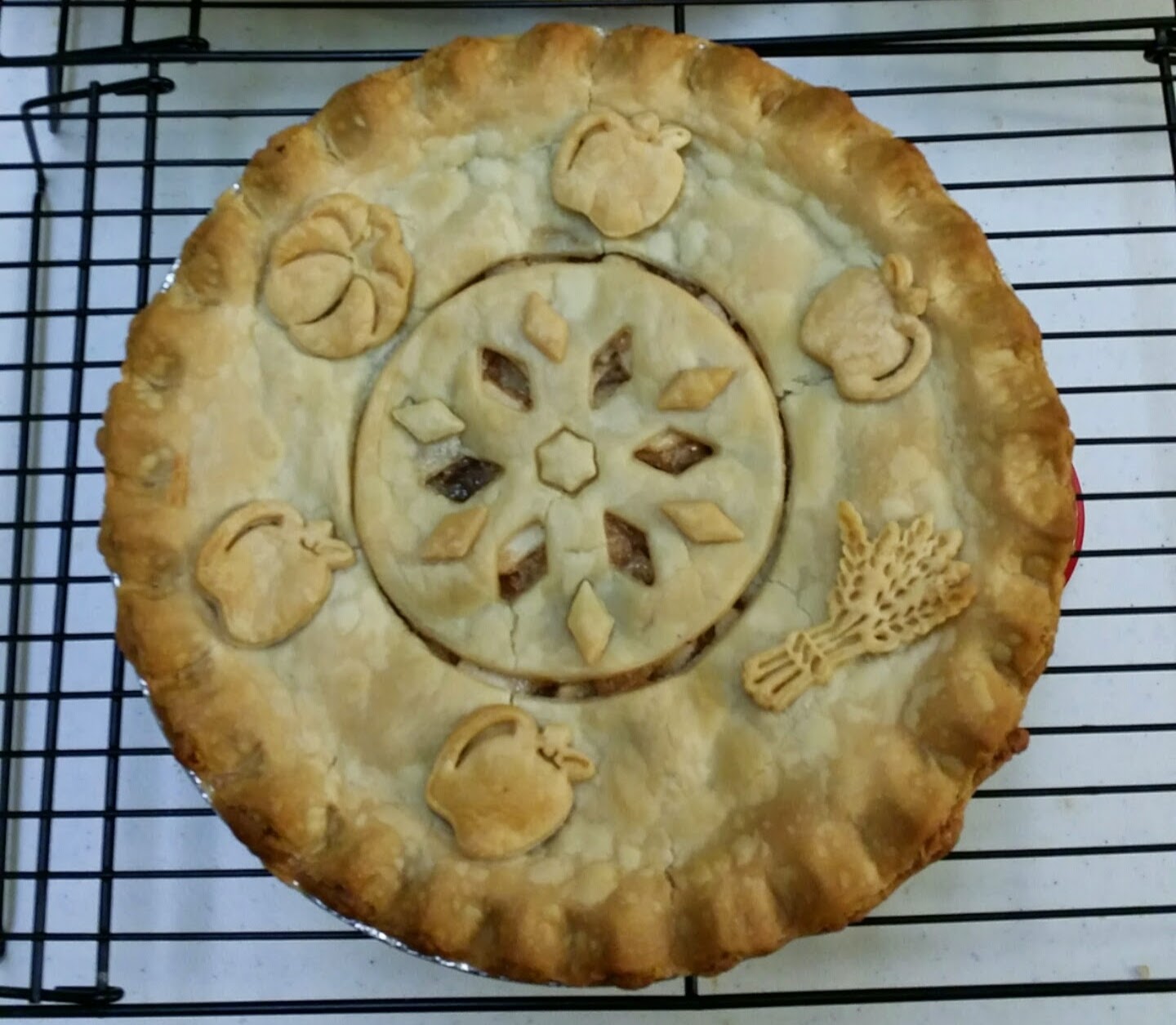 A full-sized 9-inch apple pie with decorative crust cutouts on a cooling rack