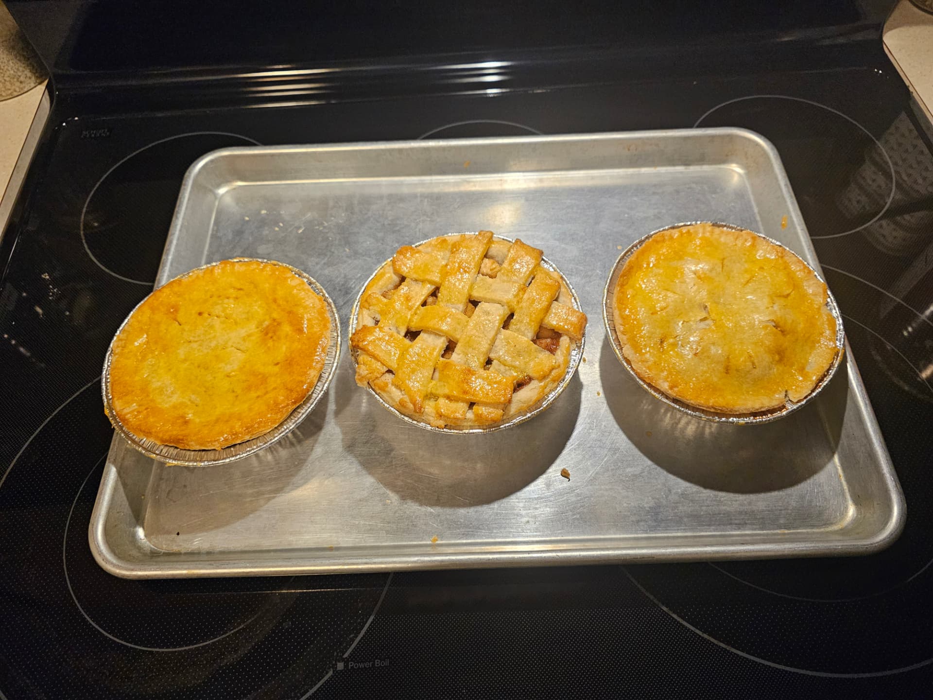 Three golden mini apple pies on a baking tray, including one with a lattice top